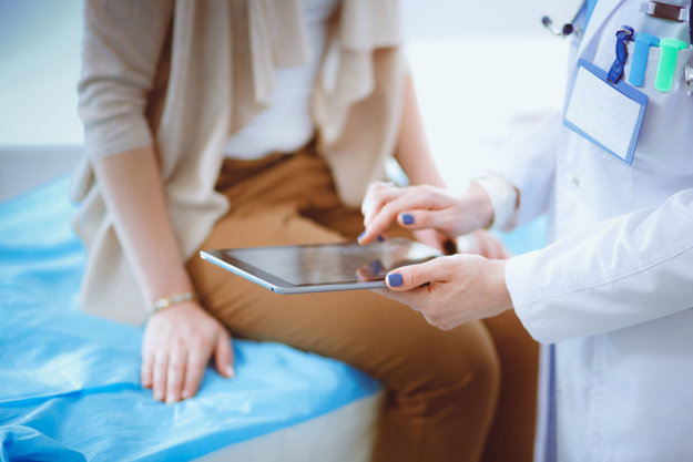 patient sitting on doctor's bed while doctor shows them an alcohol detox timeline on an ipad